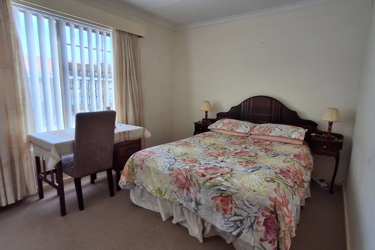 A carpeted bedroom featuring a large window with vertical blinds and coved ceiling detailing.