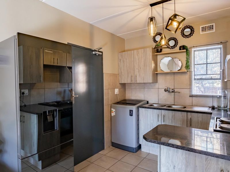 A functional kitchen featuring wood-look cabinetry, granite countertops, a double basin sink, and a built-in electric hob with tiled finishes.