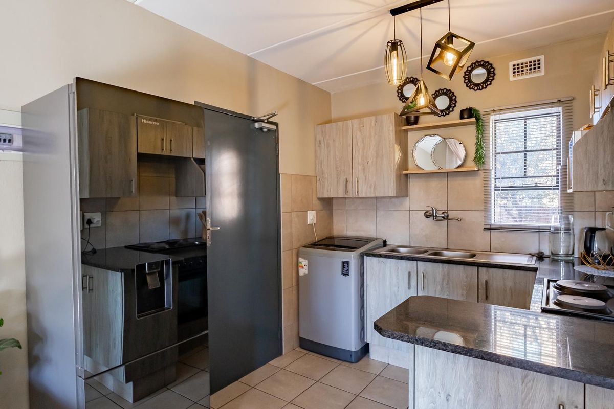 A functional kitchen featuring wood-look cabinetry, granite countertops, a double basin sink, and a built-in electric hob with tiled finishes.