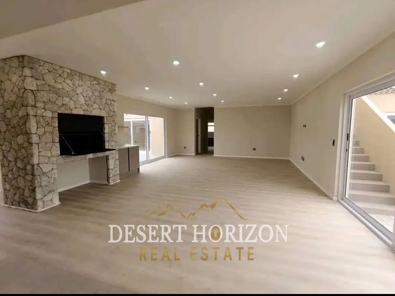 Spacious open-plan living area featuring modern laminate flooring, recessed lighting, and a striking stone-clad fireplace, with direct access to outdoor spaces.