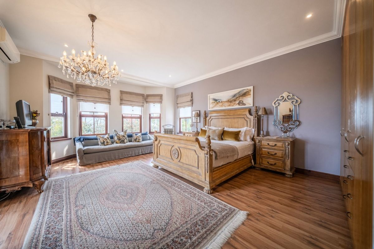 Spacious bedroom featuring laminate flooring, built-in cupboards, a bay window, and elegant chandelier lighting, creating a comfortable and well-maintained living space.