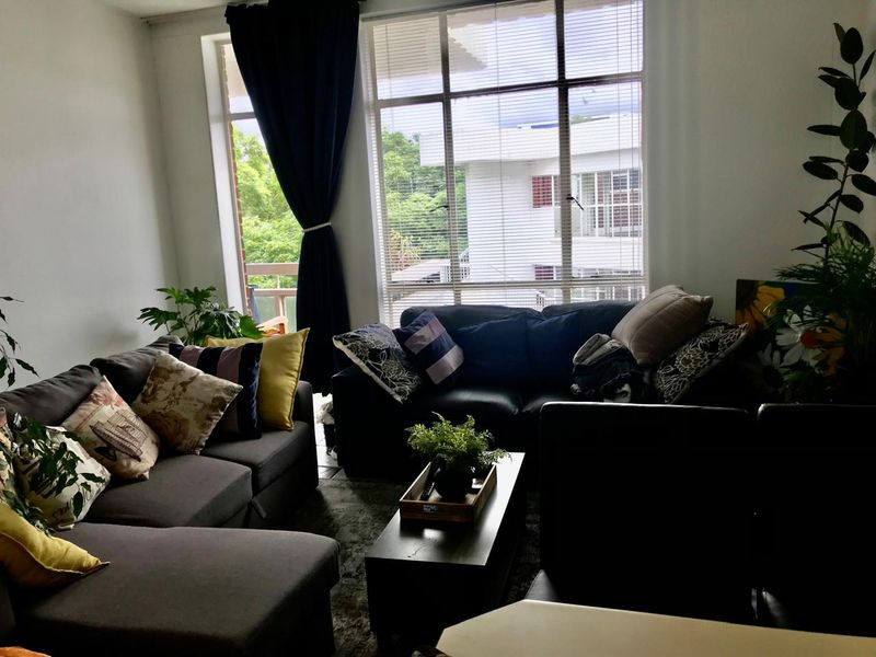 A comfortable living room featuring a large window with venetian blinds, providing natural light and a view of the surrounding area.