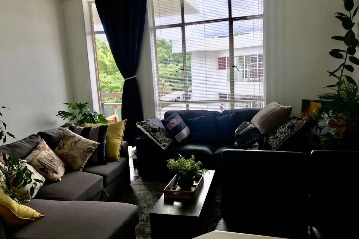 A comfortable living room featuring a large window with venetian blinds, providing natural light and a view of the surrounding area.
