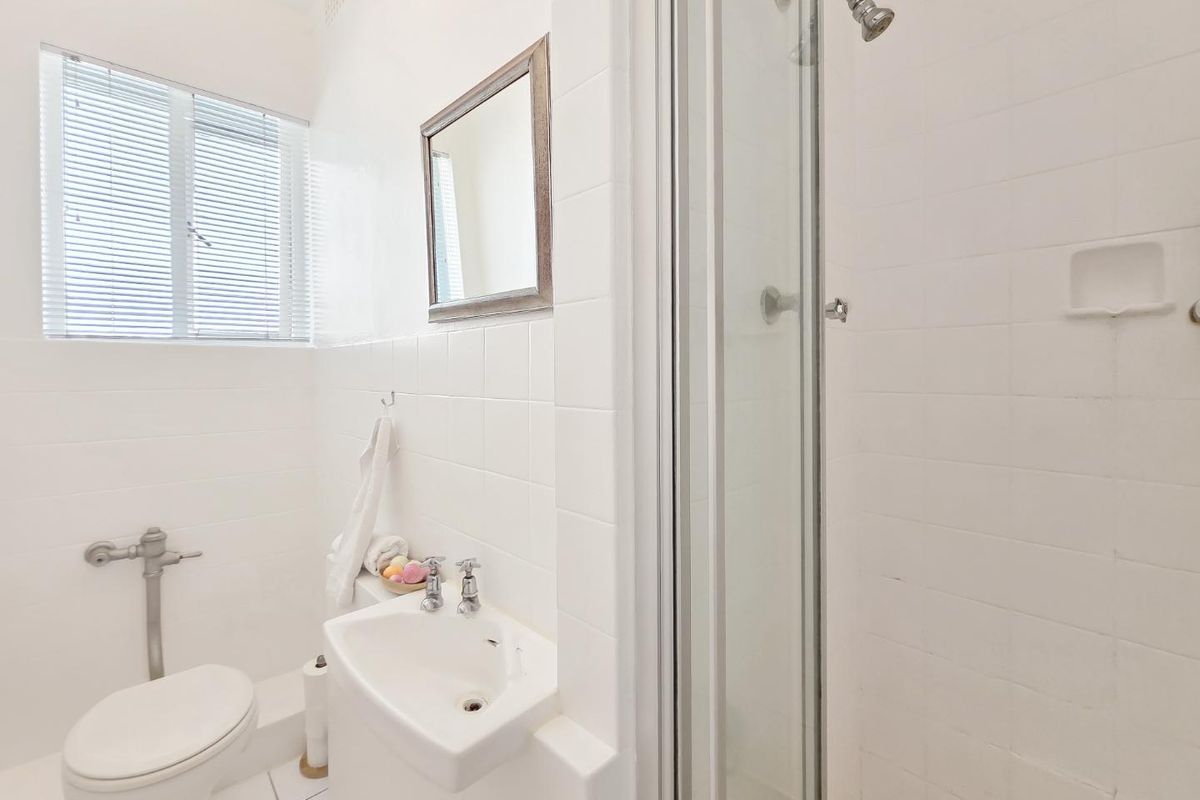 A functional bathroom featuring a shower enclosure, pedestal basin, and toilet with white tiled finishes throughout.