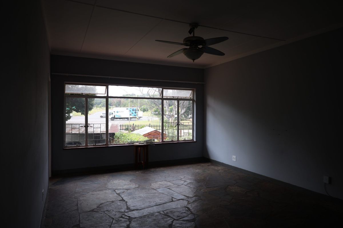 An empty living room featuring natural stone flooring, a ceiling fan, and a large window providing natural light and street views.