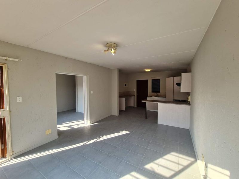 An open-plan living and kitchen area featuring tiled flooring, a breakfast bar, and functional kitchen cabinetry in a neutral, well-lit space.