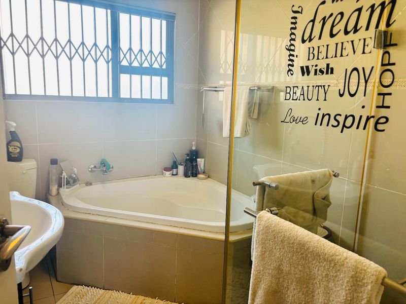 A functional bathroom featuring a corner bathtub, pedestal basin, toilet, and tiled finishes, equipped with security bars on the window.