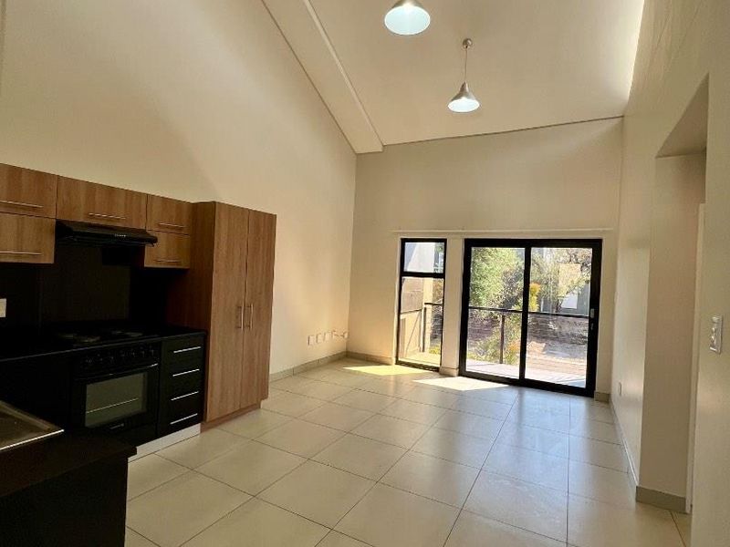 Spacious open-plan living area featuring a modern kitchen with built-in appliances, high vaulted ceilings, and large sliding doors leading to an outdoor space.