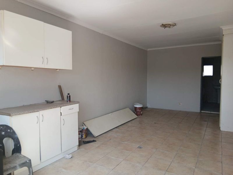 An empty kitchen area featuring basic white cabinetry, laminate countertops, and tiled flooring, currently undergoing minor maintenance or renovation.