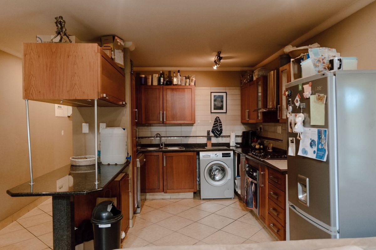 Functional kitchen featuring wood-finish cabinetry, granite countertops, integrated appliances including a washing machine, and tiled flooring with a neutral backsplash.