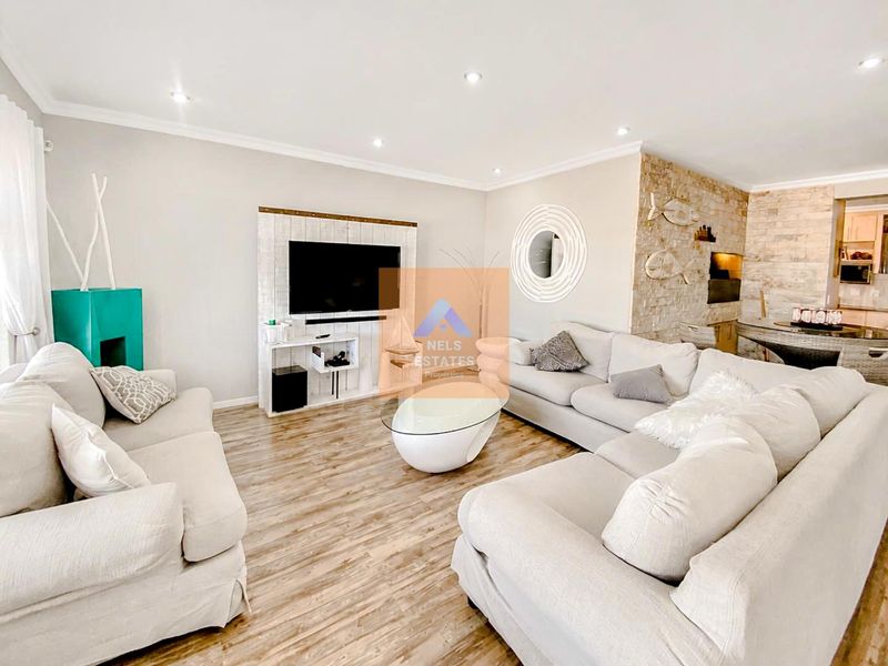 Spacious living room featuring a stone accent wall, recessed downlighting, and modern laminate flooring, creating a bright and inviting atmosphere.