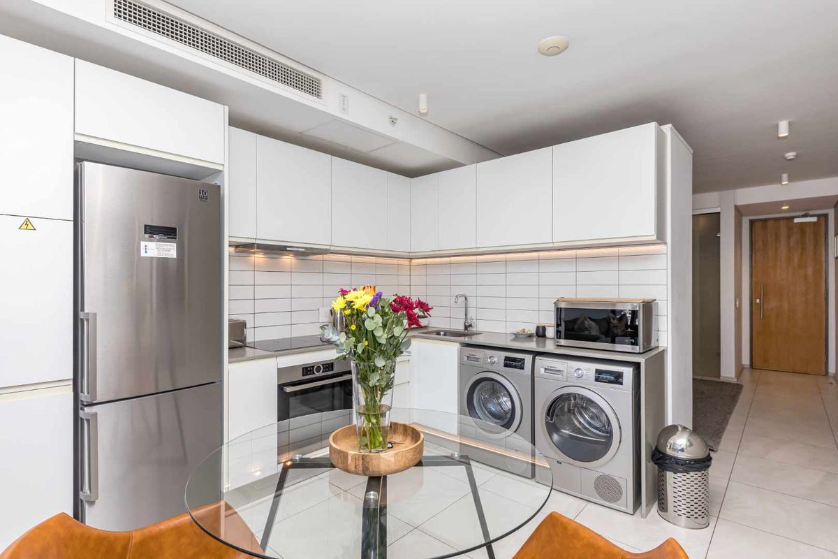 Modern kitchen featuring white cabinetry, stainless steel appliances, tiled backsplash, and integrated laundry facilities in a clean, contemporary apartment layout.