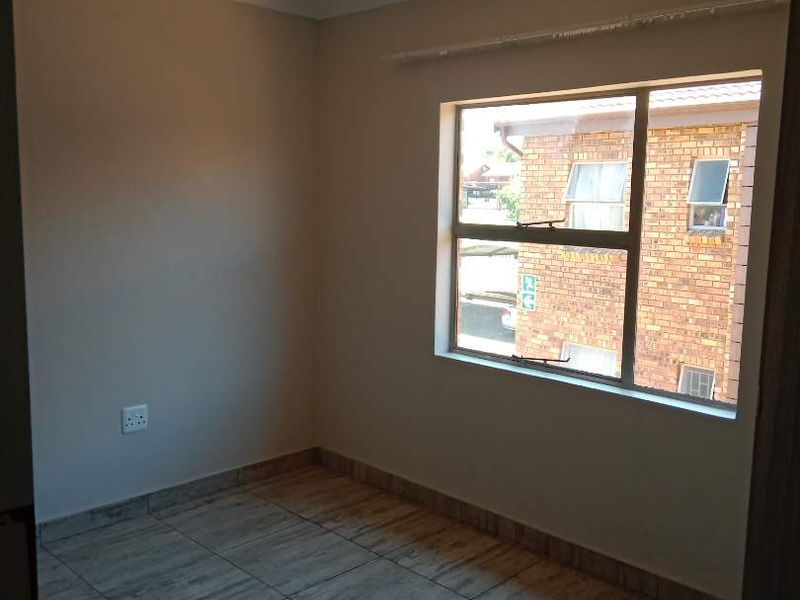 A clean, empty bedroom featuring neutral wall paint, tiled flooring, and a large window providing natural light.