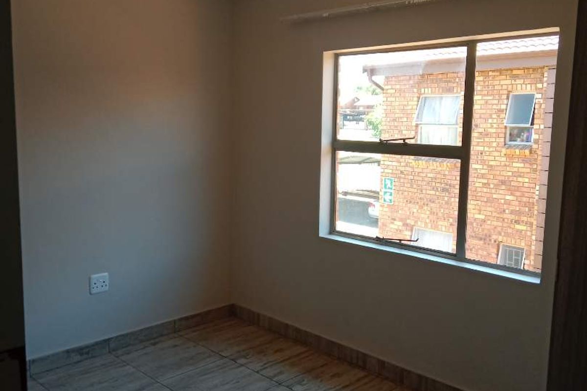 A clean, empty bedroom featuring neutral wall paint, tiled flooring, and a large window providing natural light.