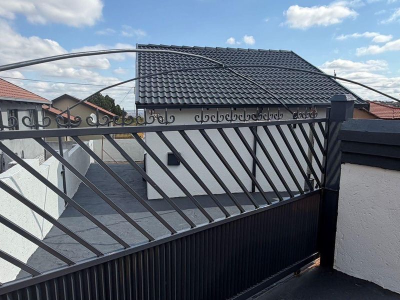 A view of the property entrance featuring a secure metal driveway gate, paved driveway, and a well-maintained tiled roof structure.