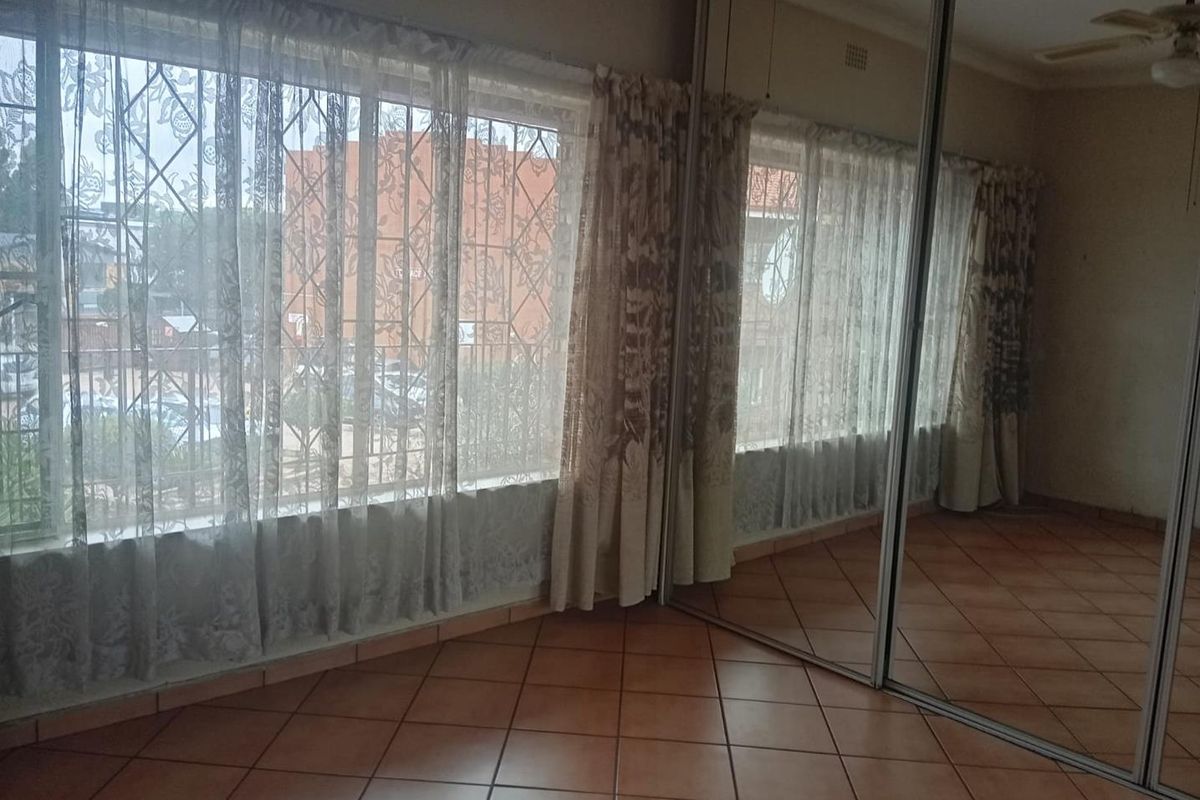 A bedroom featuring large windows with security bars, tiled flooring, and a full-length mirrored built-in wardrobe.