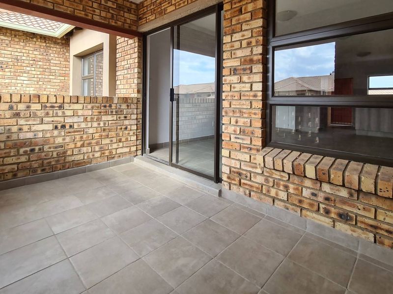 A covered patio area featuring face brick walls, tiled flooring, and a sliding glass door providing access to the interior living space.