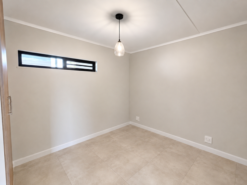 A clean, neutral-toned bedroom featuring tiled flooring, a modern pendant light, and a horizontal clerestory window, providing a bright and versatile living space.