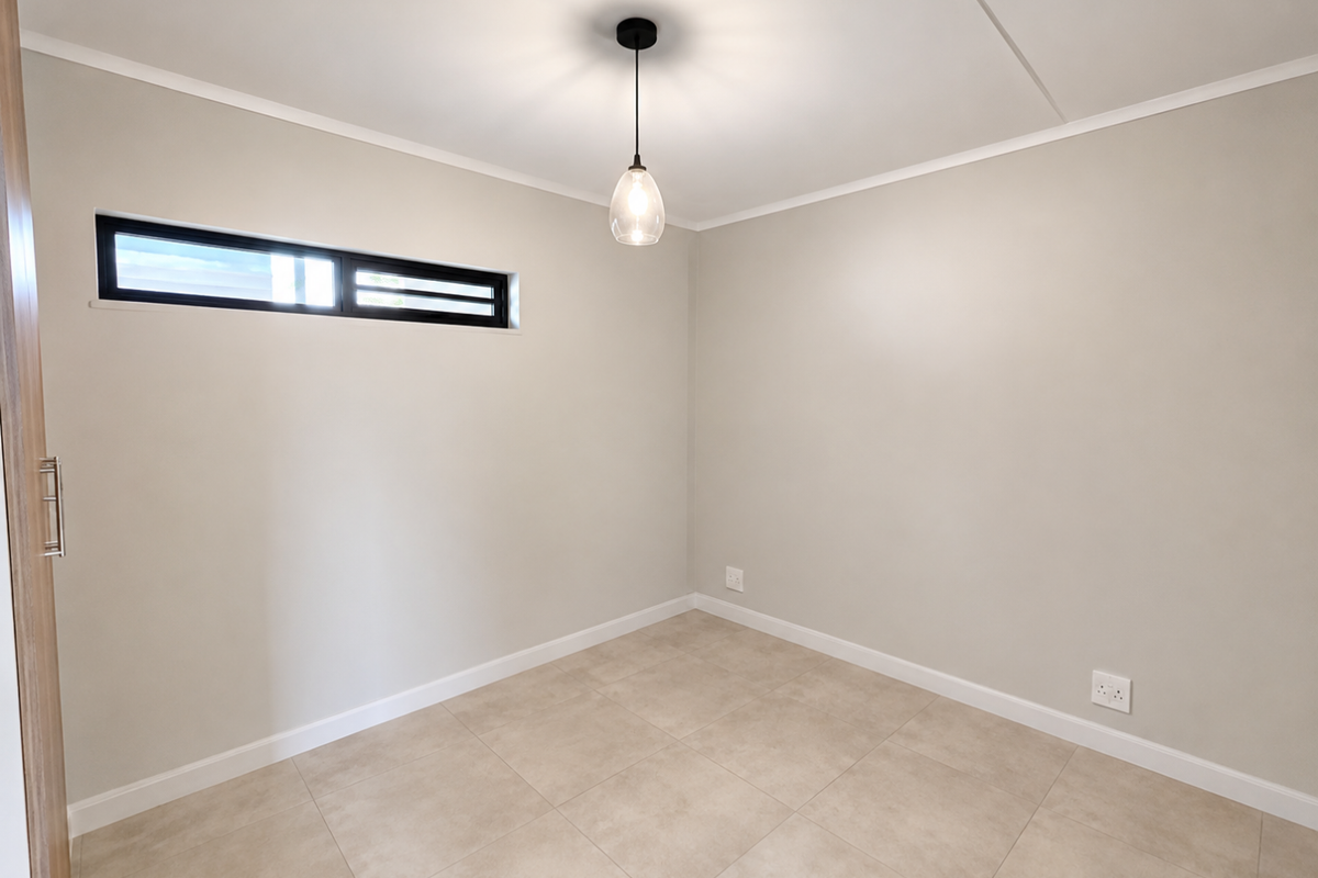 A clean, neutral-toned bedroom featuring tiled flooring, a modern pendant light, and a horizontal clerestory window, providing a bright and versatile living space.