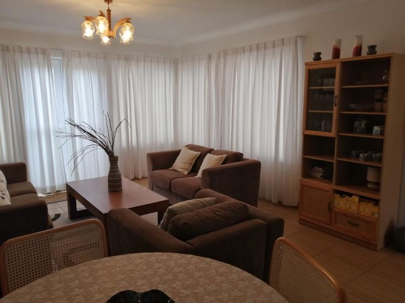 An open-plan living and dining area featuring tiled flooring and large windows covered by floor-to-ceiling curtains, providing a bright and functional space.