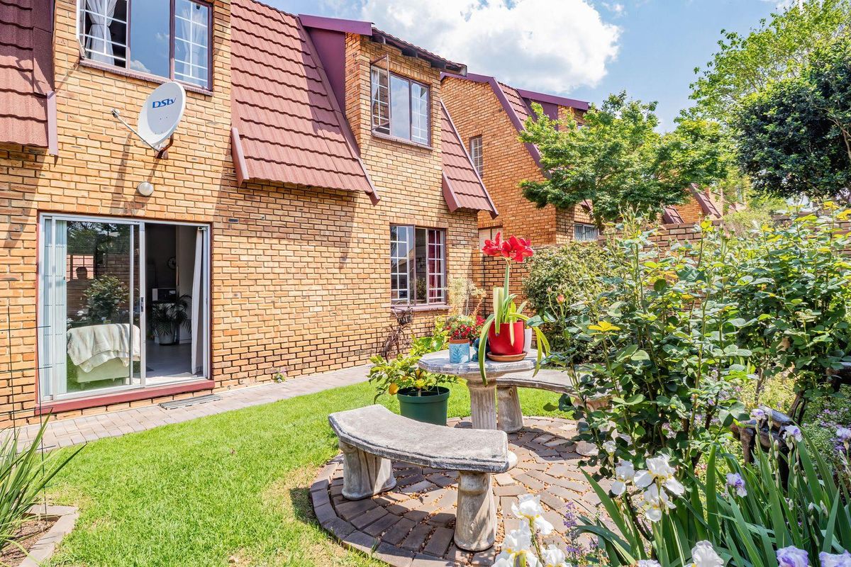 Rear view of a face brick townhouse featuring a paved patio area, landscaped garden, and sliding door access to the interior living space.