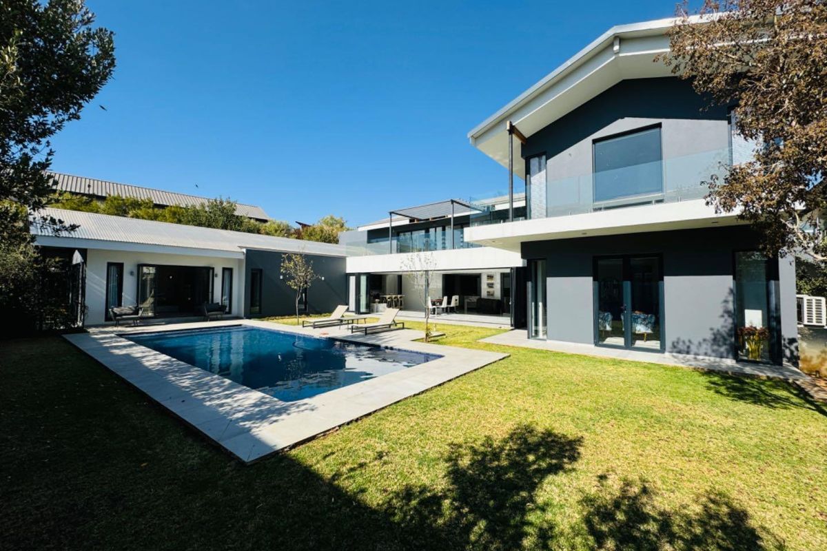 A modern architectural home featuring a swimming pool, landscaped garden, and expansive glass sliding doors connecting indoor and outdoor living spaces.