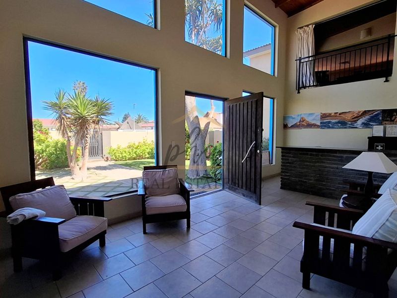 Spacious living area featuring double-volume ceilings, large windows providing natural light, tiled flooring, and a mezzanine balcony overlooking the space.