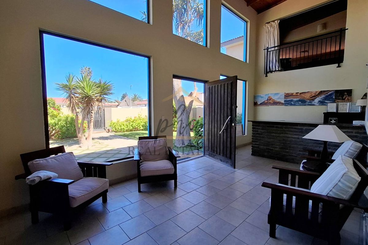 Spacious living area featuring double-volume ceilings, large windows providing natural light, tiled flooring, and a mezzanine balcony overlooking the space.