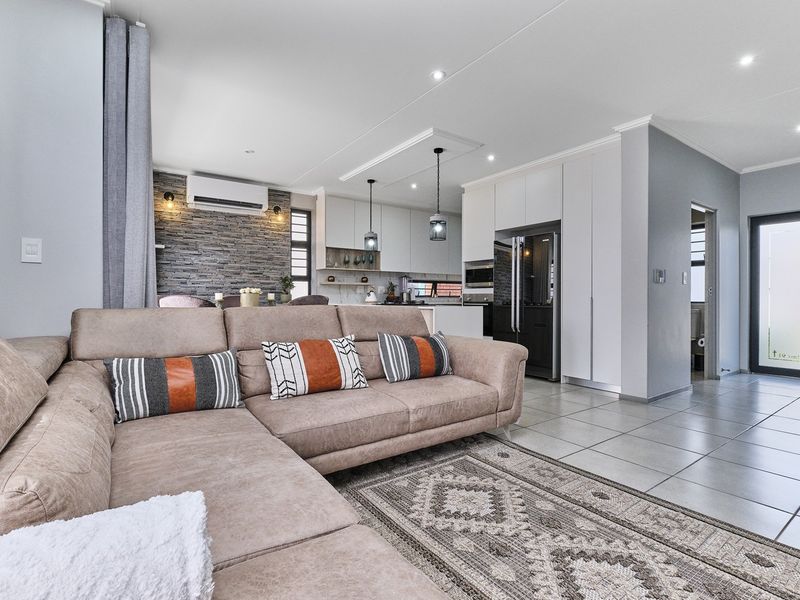 Modern open-plan living area featuring a stone accent wall, sleek white cabinetry, tiled floors, and integrated kitchen appliances in a well-maintained space.