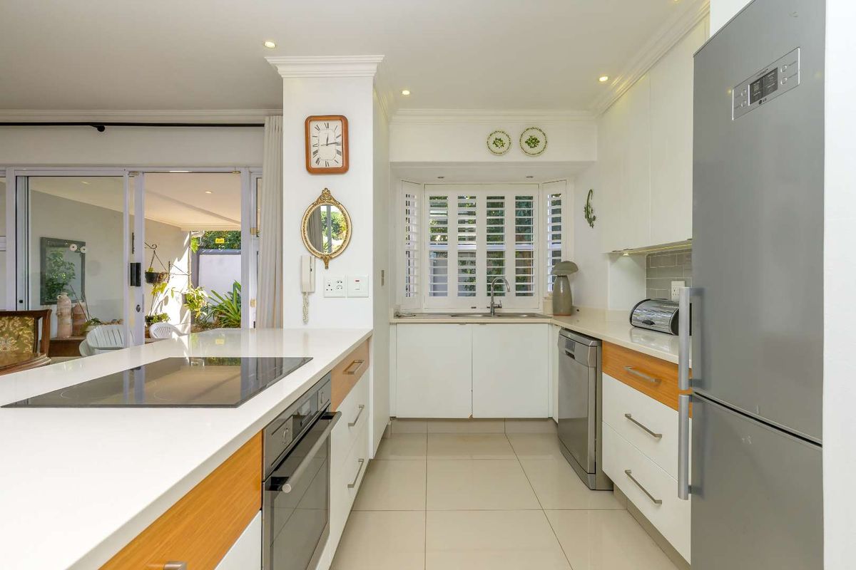 Modern kitchen featuring white cabinetry, stone countertops, integrated hob and oven, and plantation shutters, seamlessly flowing into the adjacent living area.