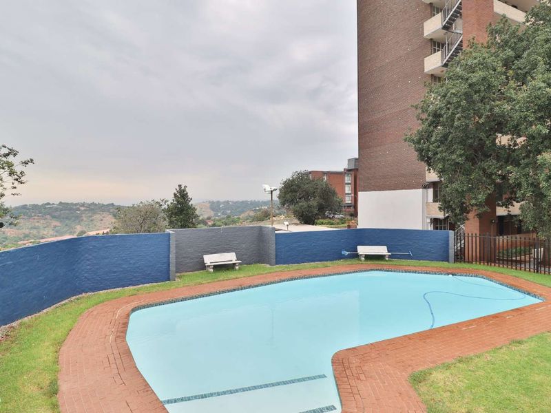 Communal swimming pool area featuring a brick-edged pool, painted masonry boundary walls, and views of the surrounding landscape.