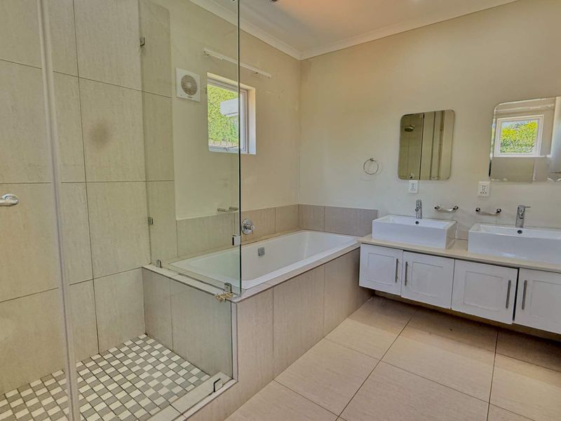A clean, modern bathroom featuring a glass-enclosed shower, a built-in bathtub, and a double vanity with contemporary sinks.