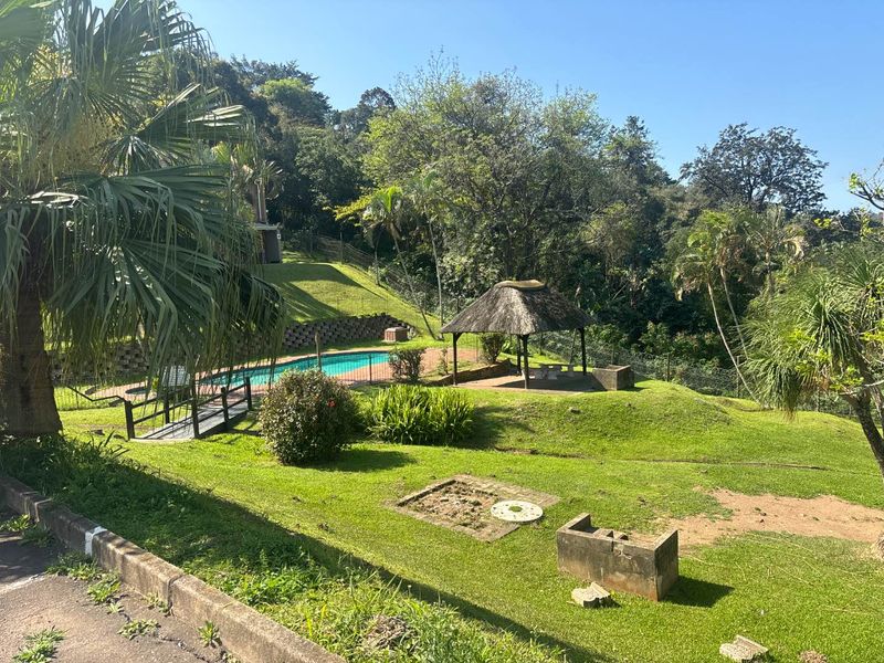 Outdoor pool area featuring a swimming pool, a thatched gazebo, and landscaped garden space with retaining walls and perimeter fencing.