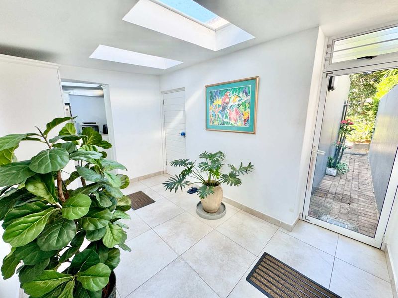 Bright entrance hall featuring large skylights, neutral tiled flooring, and direct access to an outdoor paved area through a glass panel door.