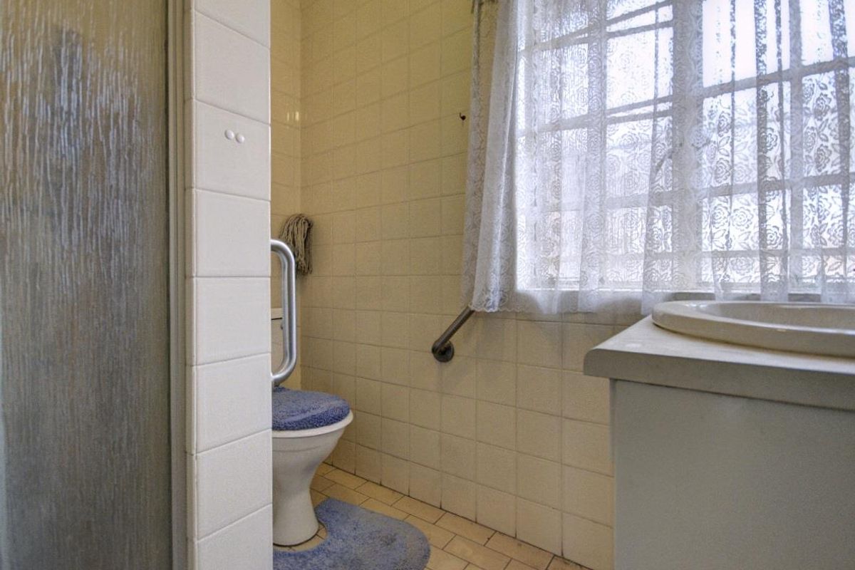 A functional bathroom featuring a shower enclosure, toilet with safety grab rail, and a built-in vanity basin with tiled finishes.