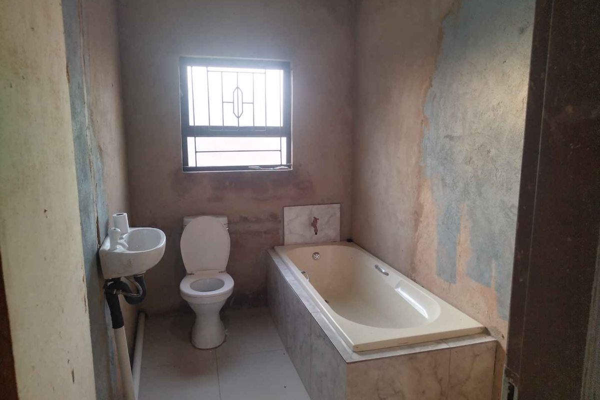 A basic bathroom featuring a built-in bathtub, toilet, and wall-mounted basin, currently requiring significant wall finishing and cosmetic updates.