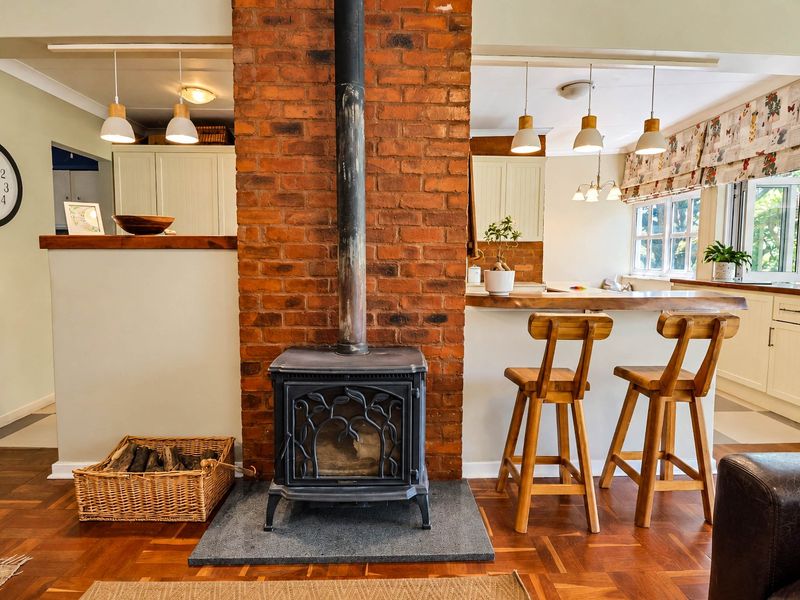 Open plan living and kitchen area featuring a prominent exposed brick fireplace with a wood burning stove and warm parquet flooring.