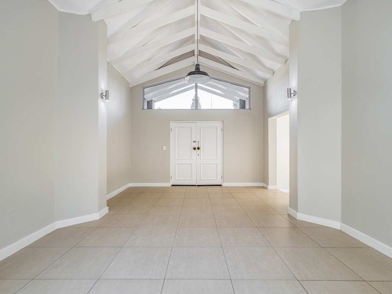Spacious entrance hall featuring a high vaulted ceiling with exposed rafters, tiled flooring, and a large double door with a transom window.