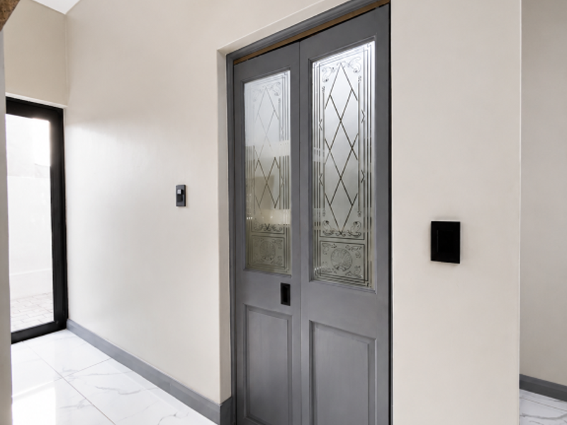 A bright, modern hallway featuring elegant double doors with decorative glass inserts and polished marble-look floor tiles.