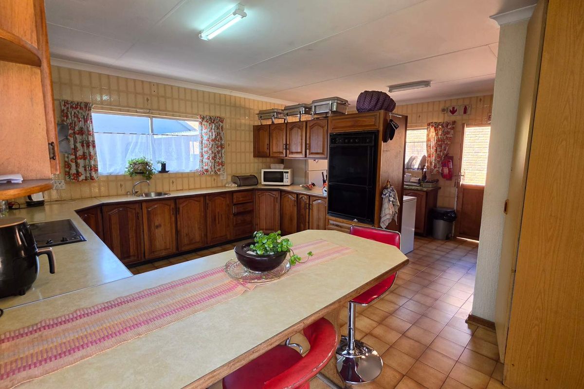 A spacious, dated kitchen featuring extensive wooden cabinetry, a double wall oven, tiled backsplash, and a central breakfast bar area with tiled flooring.