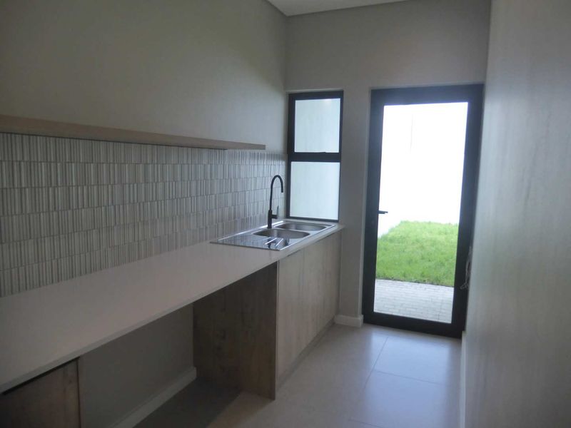 A modern, clean scullery featuring built-in cabinetry, a double sink with a mixer tap, tiled splashback, and direct access to the rear garden.