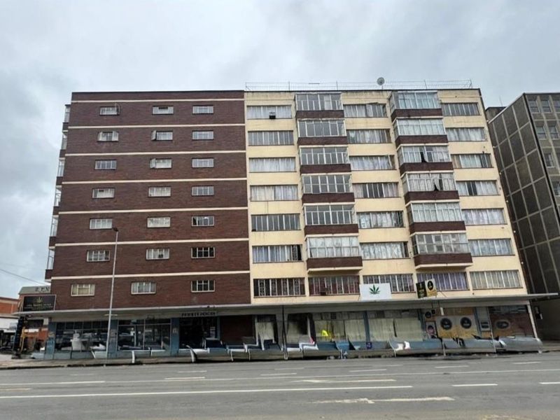 A multi-story commercial office building featuring a brick facade, enclosed balconies, and ground-level retail storefronts situated along a city street.