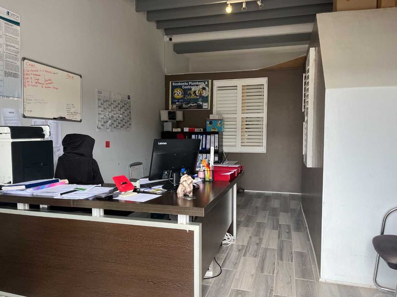 A functional office space featuring laminate flooring, exposed ceiling beams, and plantation shutters, currently utilized as a workspace.