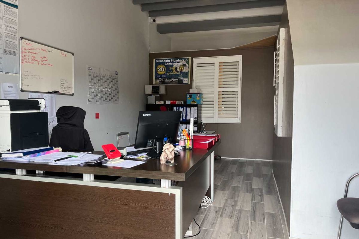 A functional office space featuring laminate flooring, exposed ceiling beams, and plantation shutters, currently utilized as a workspace.
