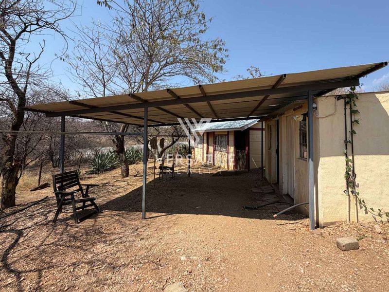 A covered outdoor patio area featuring a corrugated metal roof supported by a steel frame, adjacent to the main building structure.