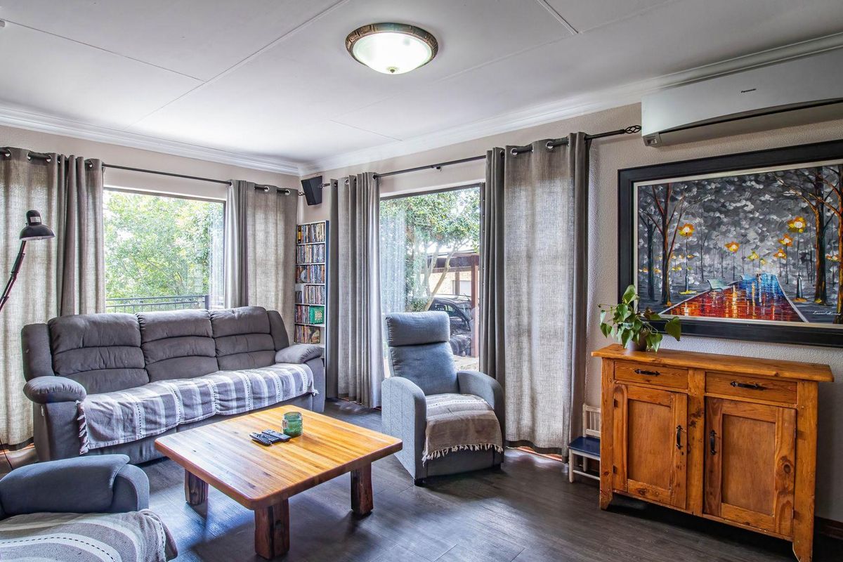 A well-maintained living room featuring laminate flooring, large windows for natural light, and a wall-mounted air conditioning unit.