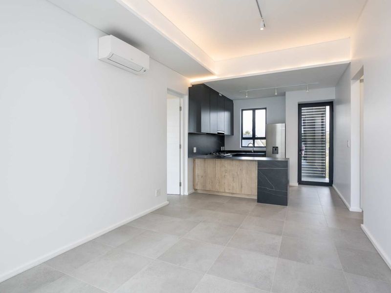 Modern open-plan living area featuring a sleek kitchen with dark cabinetry, stone countertops, integrated appliances, and neutral tiled flooring throughout.