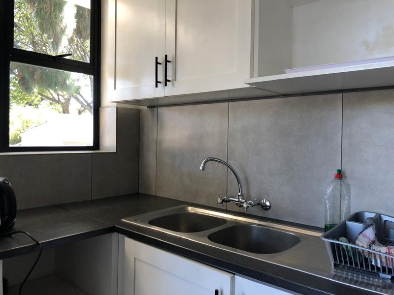A clean, modern kitchen area featuring white cabinetry, a double bowl stainless steel sink, and grey tiled backsplash with a window for natural light.