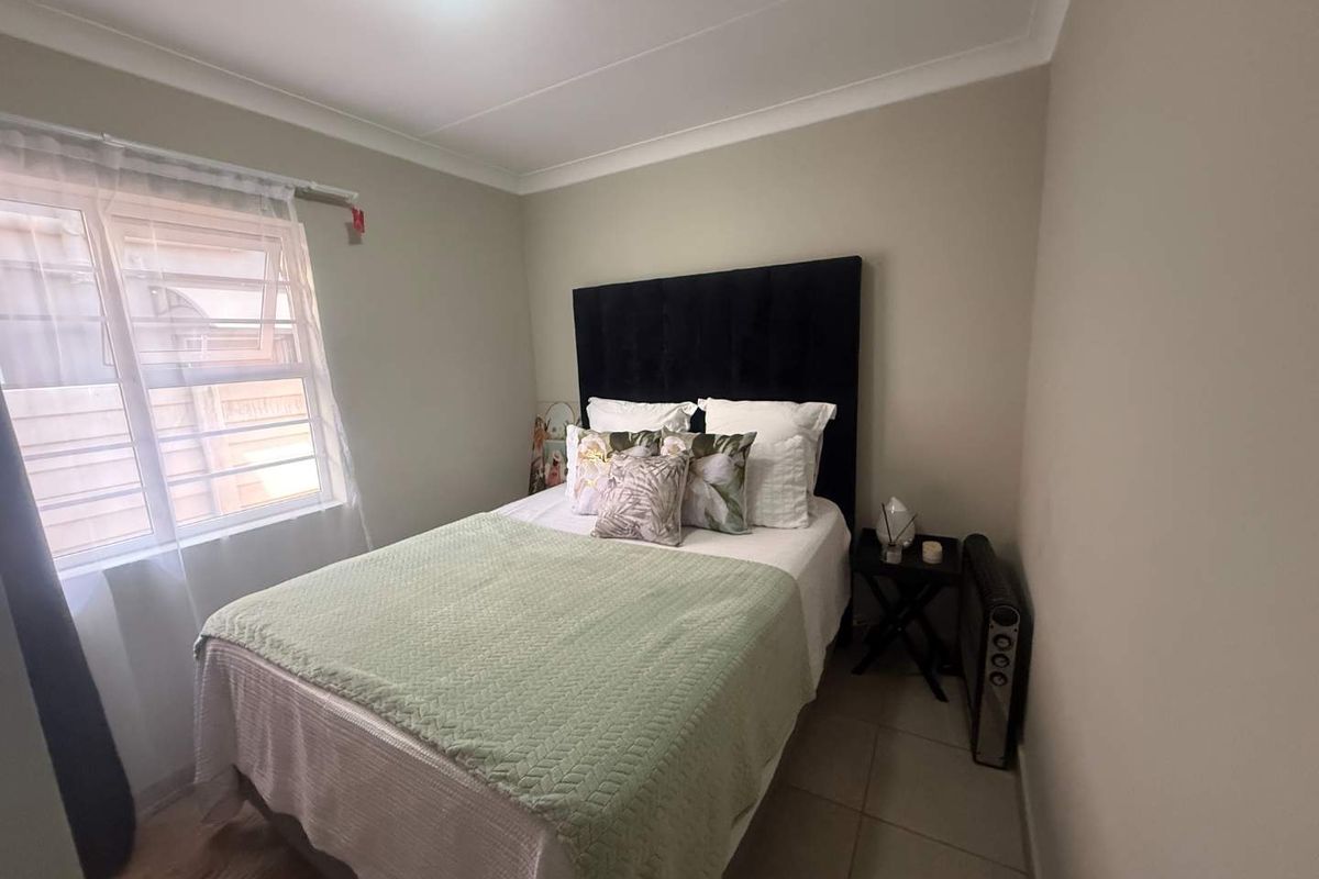 A compact bedroom featuring tiled flooring, neutral wall finishes, and a window fitted with security burglar bars.