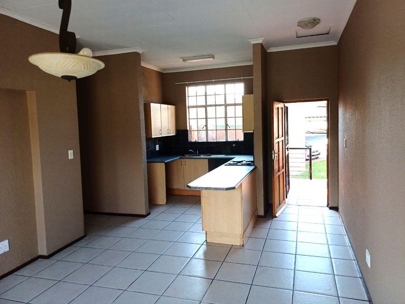 Open-plan kitchen and living area featuring tiled flooring, built-in cabinetry with laminate countertops, and direct access to an outdoor space.